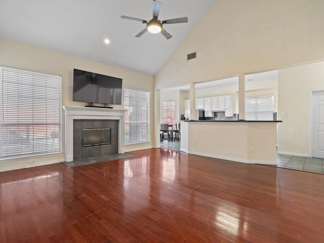 unfurnished living room featuring a tiled fireplace, wood-type flooring, a healthy amount of sunlight, and ceiling fan