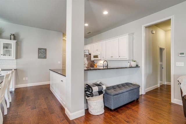 kitchen featuring dark wood-type flooring, sink, white cabinetry, dark stone countertops, and decorative backsplash