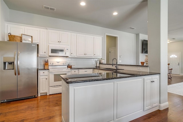 kitchen with sink, kitchen peninsula, white appliances, hardwood / wood-style floors, and white cabinets