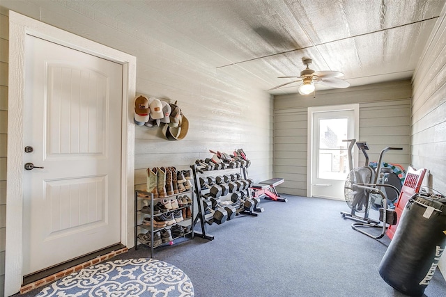 exercise area with ceiling fan, carpet flooring, and wooden walls