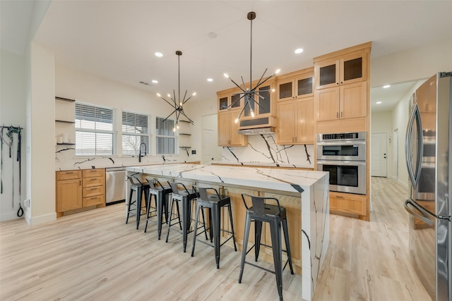 kitchen featuring appliances with stainless steel finishes, light stone counters, a large island, hanging light fixtures, and decorative backsplash