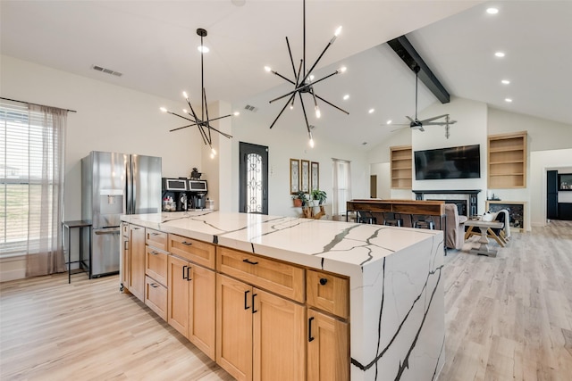 kitchen with light stone counters, stainless steel fridge, a spacious island, beamed ceiling, and light wood-type flooring