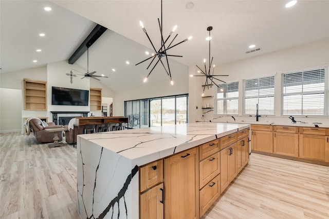 kitchen featuring beam ceiling, light stone countertops, decorative light fixtures, light hardwood / wood-style floors, and a spacious island