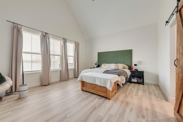 bedroom featuring high vaulted ceiling, light hardwood / wood-style flooring, and a barn door