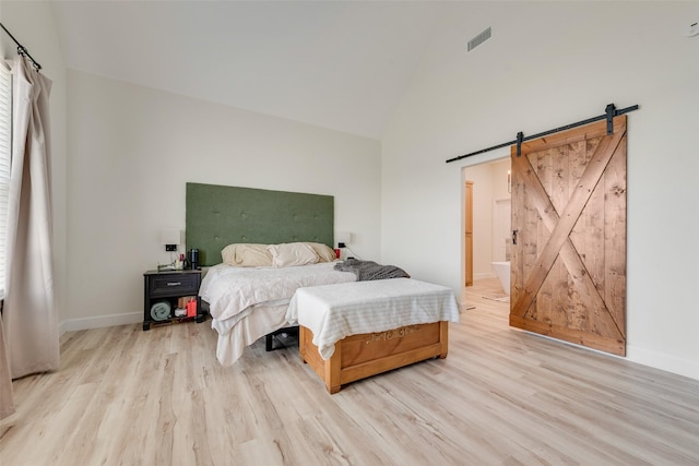 bedroom featuring high vaulted ceiling, light hardwood / wood-style flooring, ensuite bath, and a barn door