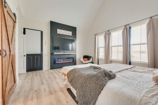 bedroom with high vaulted ceiling, light hardwood / wood-style flooring, a barn door, and a fireplace