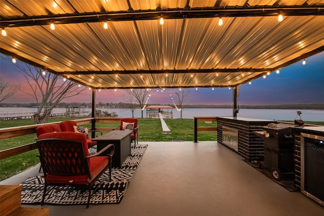 patio terrace at dusk featuring a yard, a water view, and exterior bar