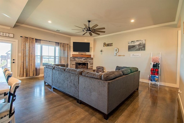 living room with dark wood-type flooring, ceiling fan, ornamental molding, and a fireplace