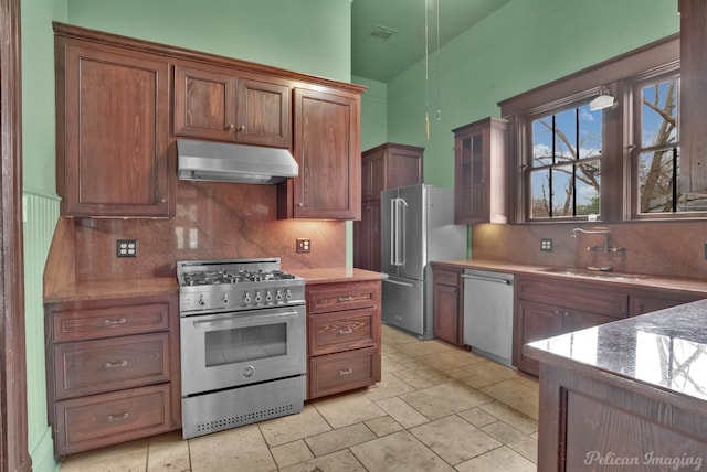 kitchen with stone counters, vaulted ceiling, tasteful backsplash, sink, and premium appliances