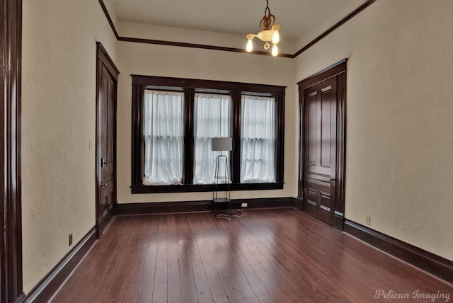 empty room featuring crown molding, a notable chandelier, and dark hardwood / wood-style flooring