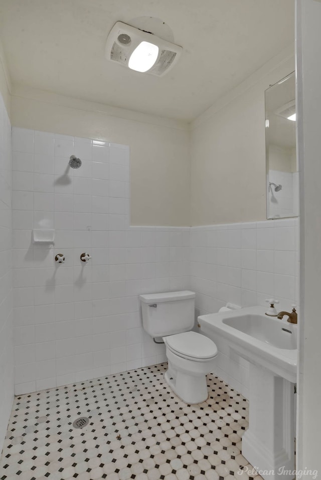 bathroom with ornamental molding, toilet, tile walls, and a tile shower