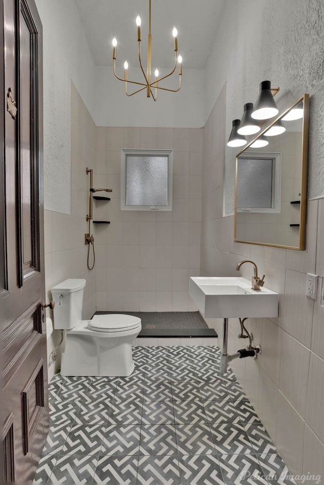 bathroom featuring sink, tile walls, tiled shower, toilet, and a chandelier