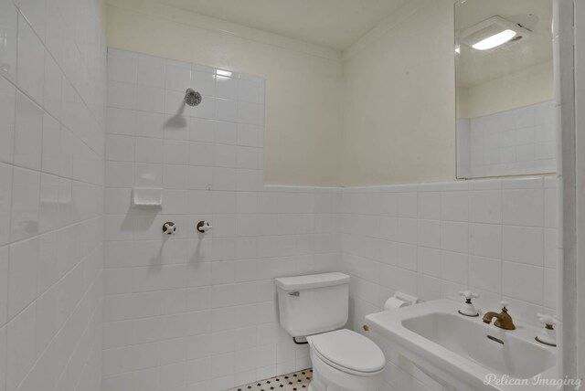 bathroom with tiled shower, toilet, sink, crown molding, and tile walls