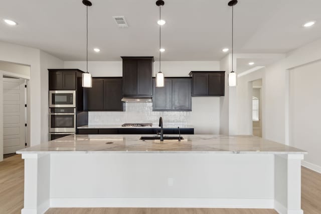 120 Bristol Ln, Azle, TX 76020 - kitchen with stainless steel appliances, a large island with sink, tasteful backsplash, light wood-style floors, and light stone countertops