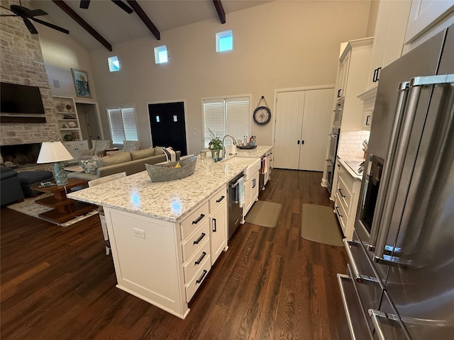 kitchen featuring dark hardwood / wood-style floors, white cabinetry, an island with sink, light stone countertops, and beam ceiling