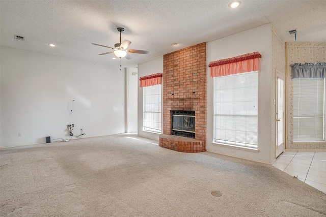 unfurnished living room featuring ceiling fan, light colored carpet, a brick fireplace, and a textured ceiling