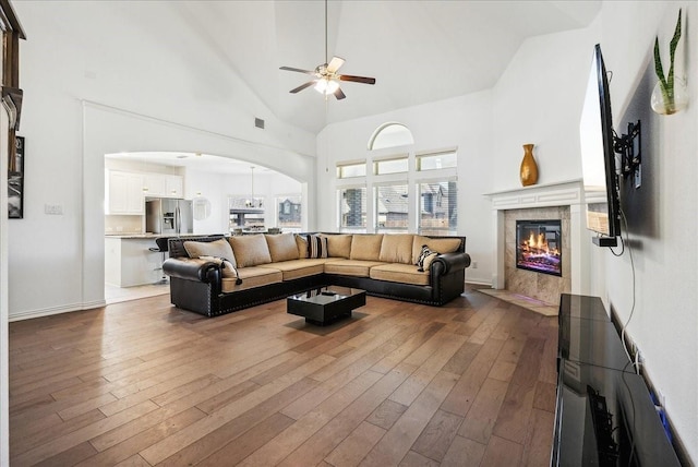 living room with ceiling fan, high vaulted ceiling, dark hardwood / wood-style floors, and a tile fireplace