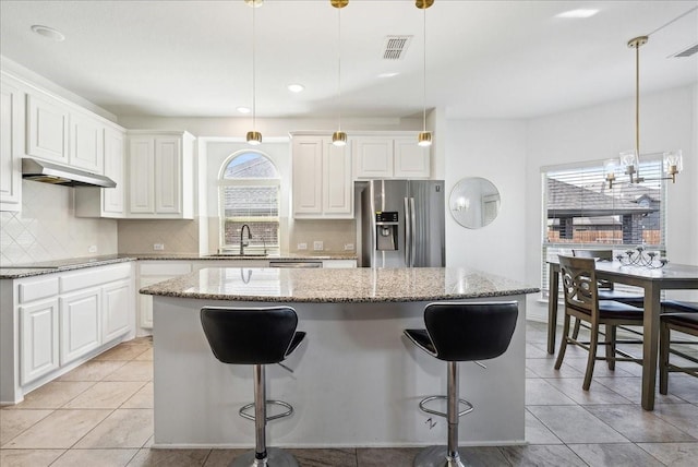 kitchen featuring stone counters, a kitchen island, pendant lighting, and stainless steel fridge