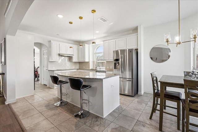 kitchen with pendant lighting, white cabinetry, stainless steel refrigerator with ice dispenser, light stone countertops, and a kitchen island