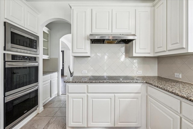 kitchen with white cabinetry, appliances with stainless steel finishes, backsplash, and dark stone counters