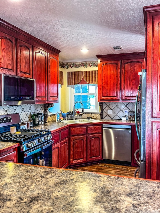 kitchen featuring sink, a textured ceiling, appliances with stainless steel finishes, dark hardwood / wood-style flooring, and decorative backsplash