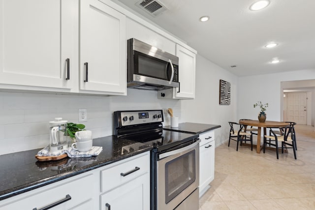 kitchen featuring tasteful backsplash, dark stone countertops, white cabinets, light tile patterned floors, and stainless steel appliances