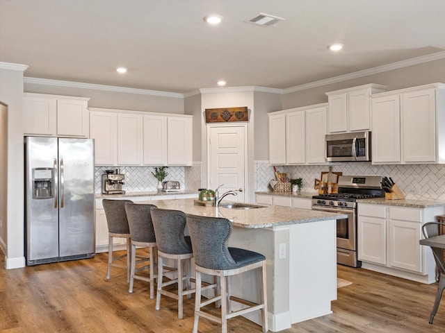2705 Colorado Dr, Little Elm, TX 75068 - kitchen with stainless steel appliances, a sink, a kitchen island with sink, white cabinetry, and ornamental molding