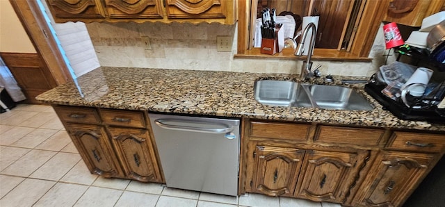 kitchen with stainless steel dishwasher, light tile patterned floors, sink, and dark stone countertops