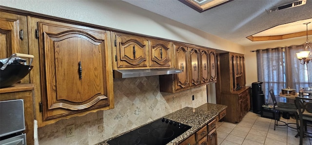 kitchen with light tile patterned floors, dark stone countertops, backsplash, a notable chandelier, and black electric stovetop