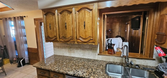 kitchen with light tile patterned flooring, sink, a textured ceiling, dark stone counters, and backsplash