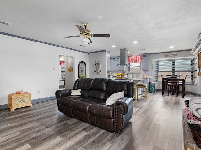 living room featuring hardwood / wood-style floors, ornamental molding, a textured ceiling, and ceiling fan