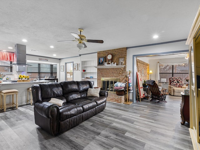 living room with crown molding, a textured ceiling, ceiling fan, a fireplace, and light hardwood / wood-style floors