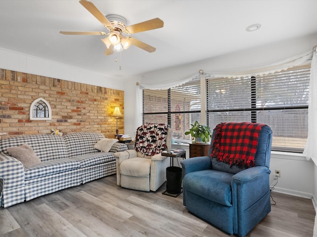 living room with light hardwood / wood-style floors, ceiling fan, and brick wall