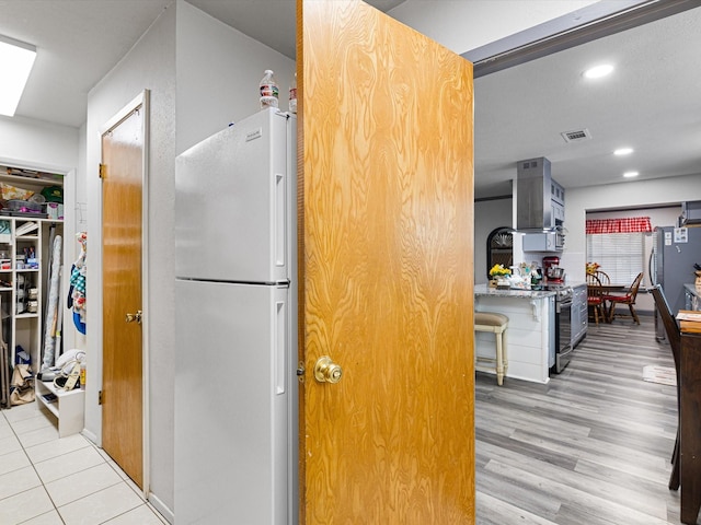 kitchen featuring appliances with stainless steel finishes, wall chimney range hood, and light hardwood / wood-style flooring