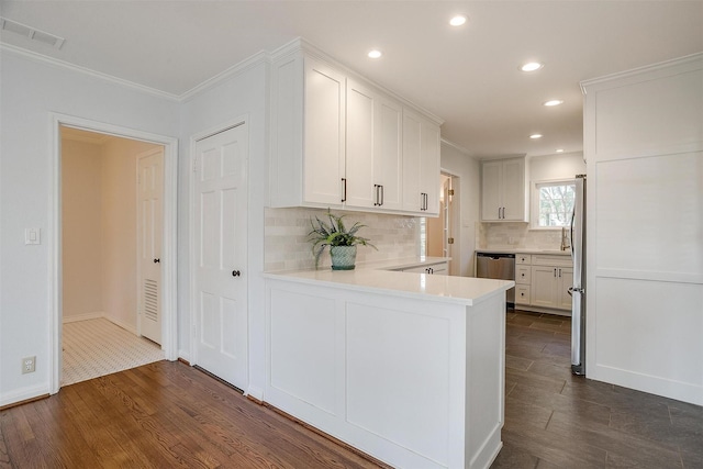 kitchen with tasteful backsplash, white cabinets, kitchen peninsula, stainless steel appliances, and dark wood-type flooring