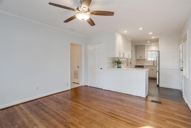 kitchen with white cabinetry, tasteful backsplash, wood-type flooring, ornamental molding, and kitchen peninsula