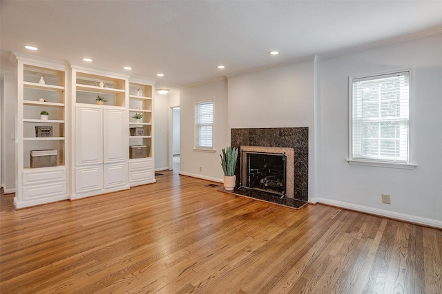 unfurnished living room with a high end fireplace, ornamental molding, and light wood-type flooring