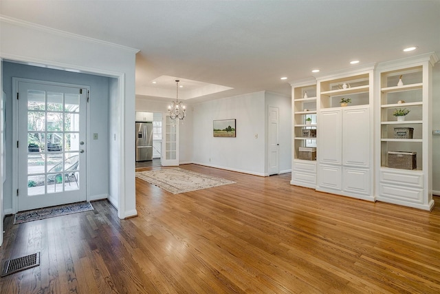 interior space with a raised ceiling, wood-type flooring, an inviting chandelier, and crown molding