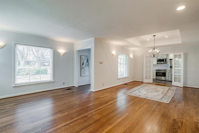 unfurnished living room featuring ornamental molding, a raised ceiling, hardwood / wood-style floors, and a notable chandelier