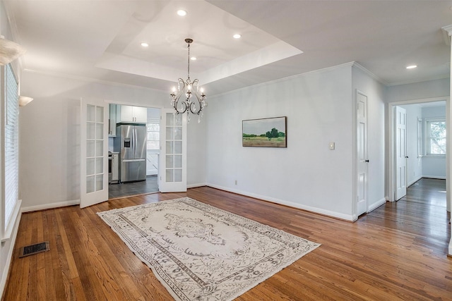 dining room featuring an inviting chandelier, dark hardwood / wood-style floors, ornamental molding, a raised ceiling, and french doors