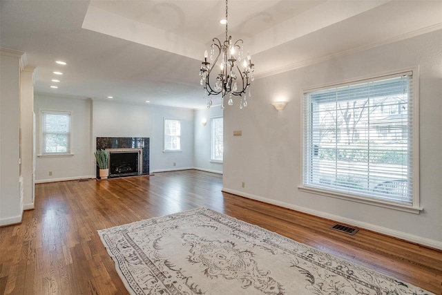 unfurnished living room with a high end fireplace, ornamental molding, wood-type flooring, a raised ceiling, and a chandelier