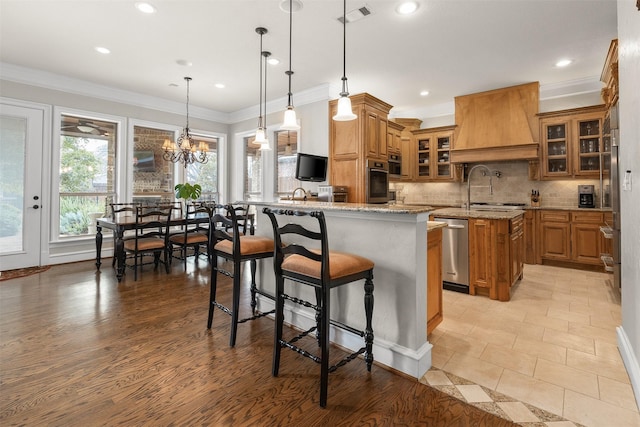 kitchen featuring hanging light fixtures, premium range hood, a breakfast bar, and light stone counters