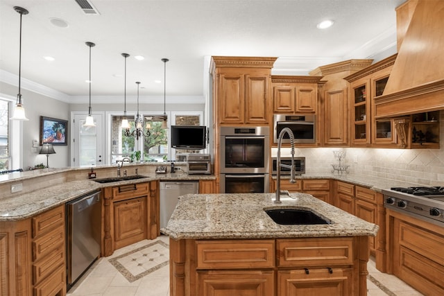 kitchen featuring appliances with stainless steel finishes, sink, hanging light fixtures, a kitchen island with sink, and light stone counters