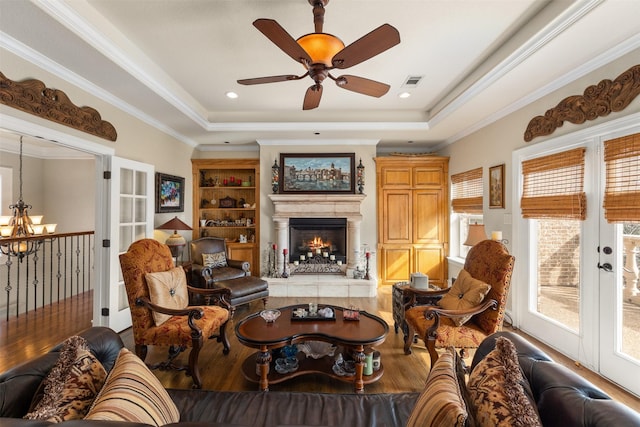 living room featuring a raised ceiling, wood-type flooring, ornamental molding, and ceiling fan with notable chandelier