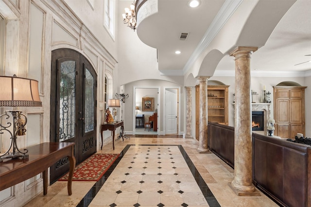 foyer entrance featuring a high end fireplace, ornamental molding, decorative columns, and french doors