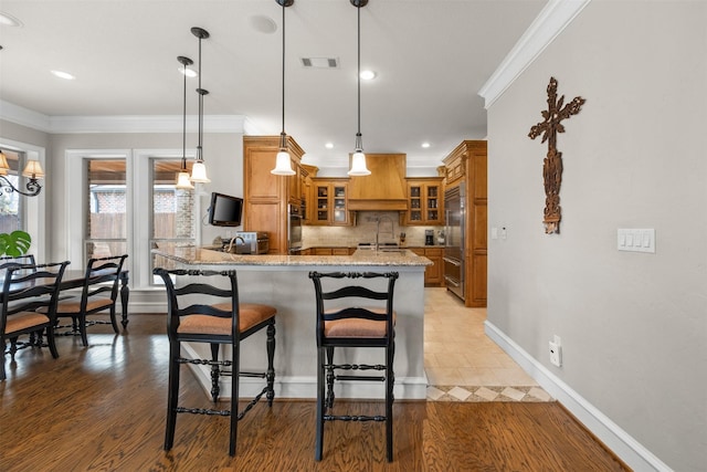 kitchen with sink, crown molding, built in refrigerator, light stone counters, and decorative light fixtures