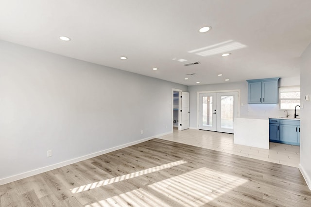 unfurnished living room featuring sink, light wood-type flooring, and french doors