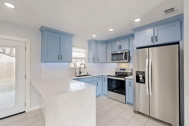 kitchen with sink, light tile patterned floors, blue cabinetry, appliances with stainless steel finishes, and light stone counters