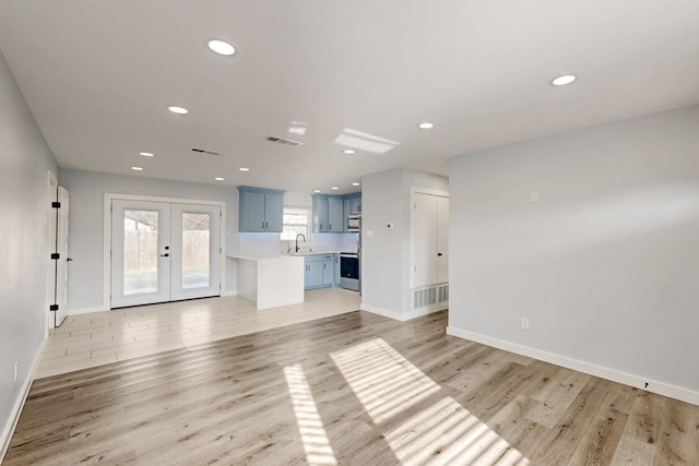 unfurnished living room featuring sink, light hardwood / wood-style floors, and french doors