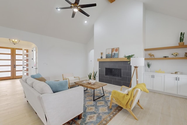 living room featuring ceiling fan, high vaulted ceiling, a fireplace, french doors, and light wood-type flooring